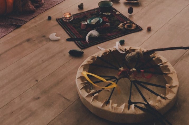 tambour chamanique avec en arrière-plan des objets rituels disposés sur un petit tapis coloré et autour de celui-ci